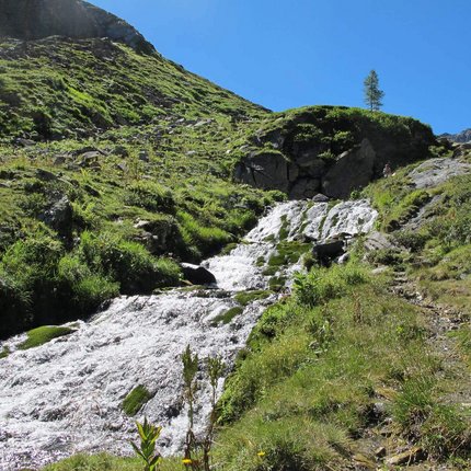 Mountain stream with waterfall and green meadows under clear blue sky