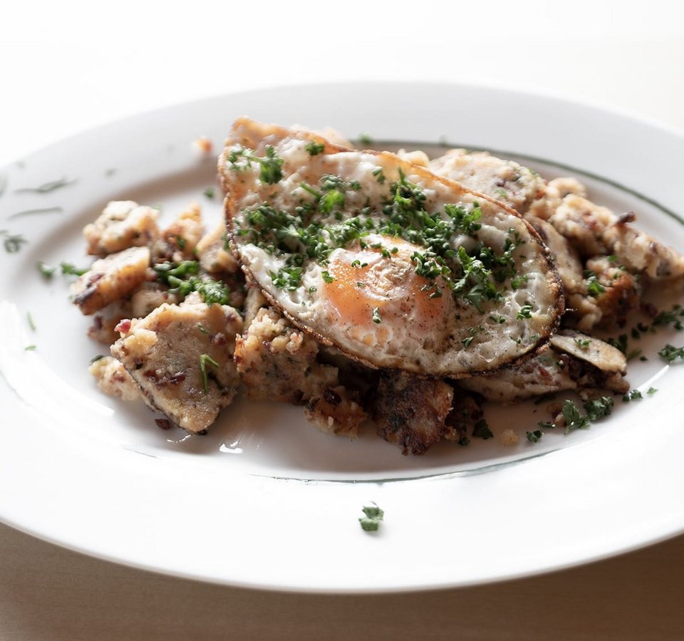 Fried potatoes with fried egg and chopped herbs on white plate