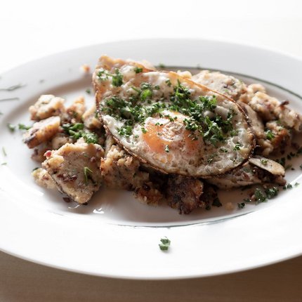Fried potatoes with fried egg and chopped herbs on white plate