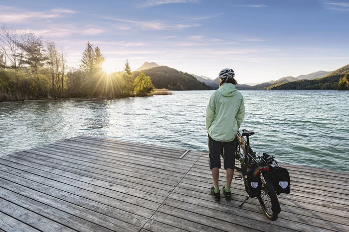 Person with bicycle on dock looking at lake at sunset
