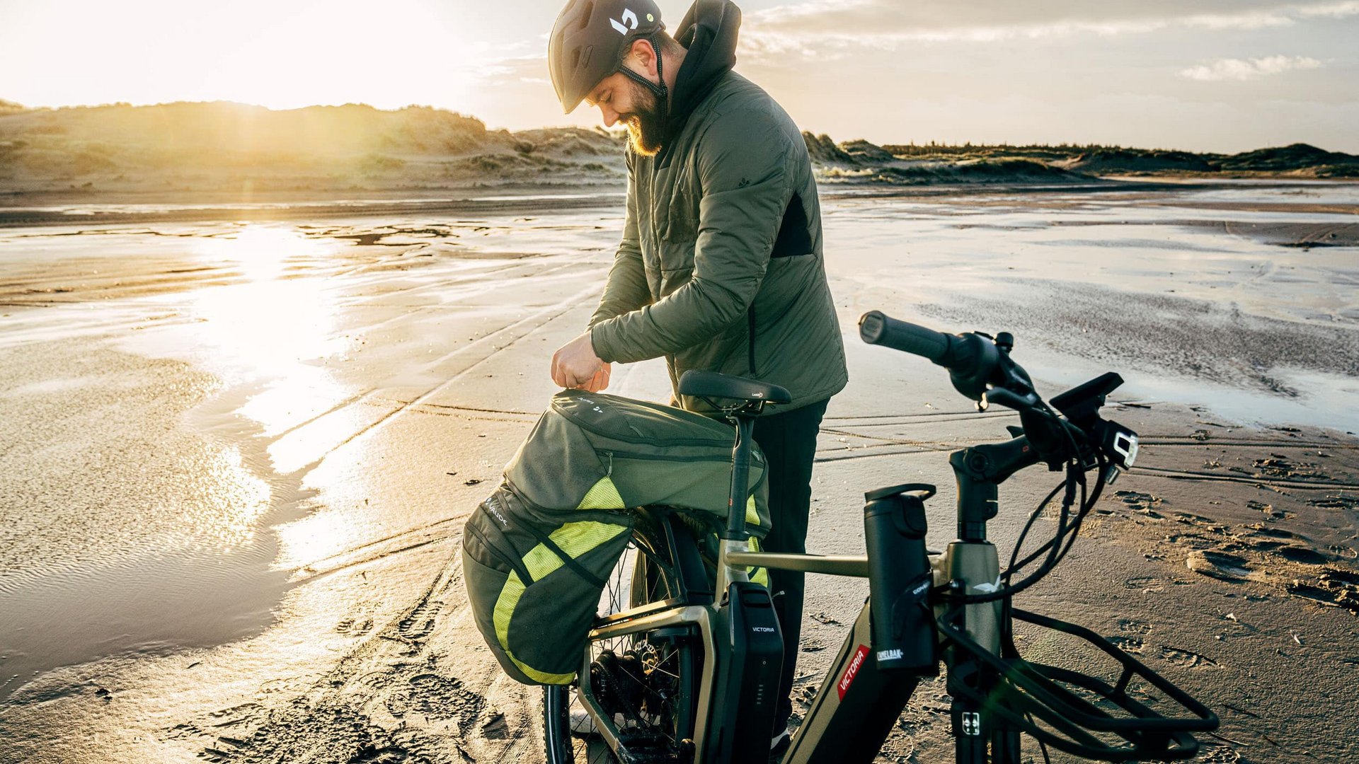 Victoria Man with helmet packing bike bag on beach at sunset