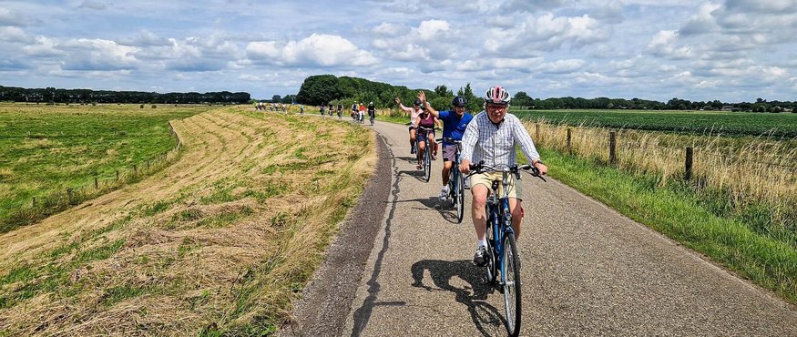 Group of cyclists riding on country road under cloudy sky