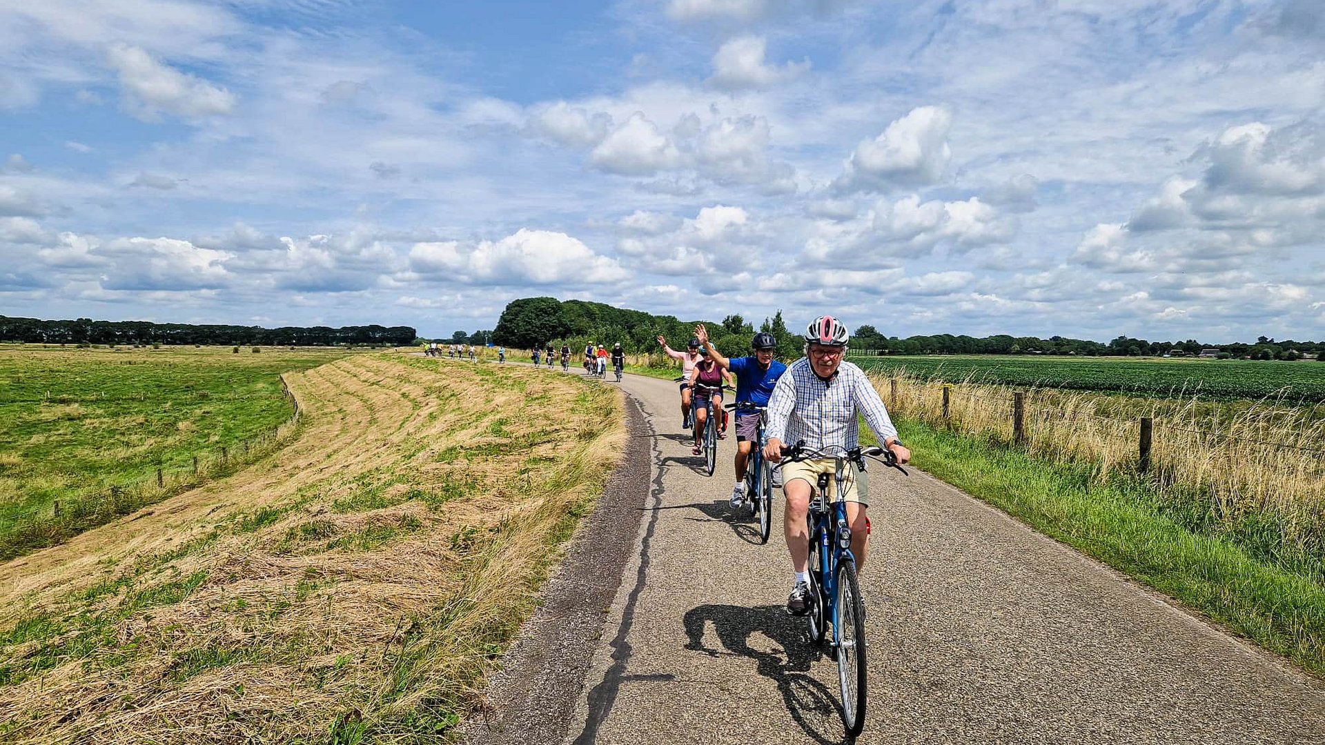 Group of cyclists riding on country road under cloudy sky