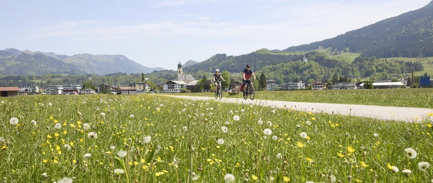 Radeln mit Weitblick im Zillertal © TVB Kufsteinerland - Simon Hausberger Zwei Radfahrer auf einem Weg durch blühende Wiesen mit Bergen im Hintergrund