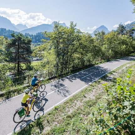 Two cyclists riding on a mountain path through a forested landscape