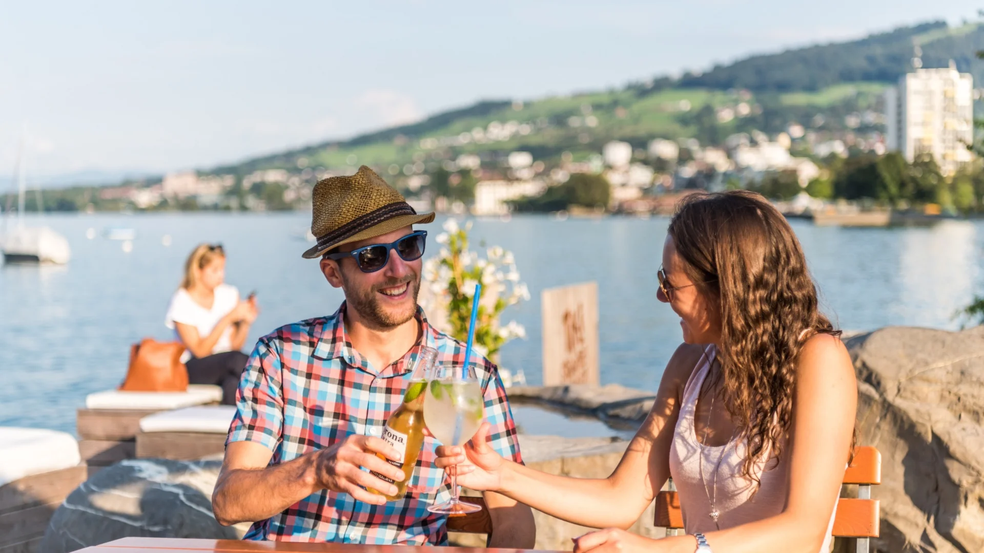 Stel tikt drankjes aan bij terras aan het meer op zonnige dag