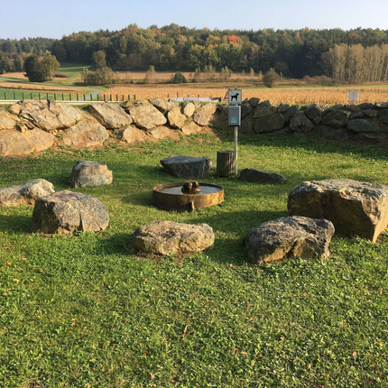 Round stone circle with water fountain on grass near stone wall and forest