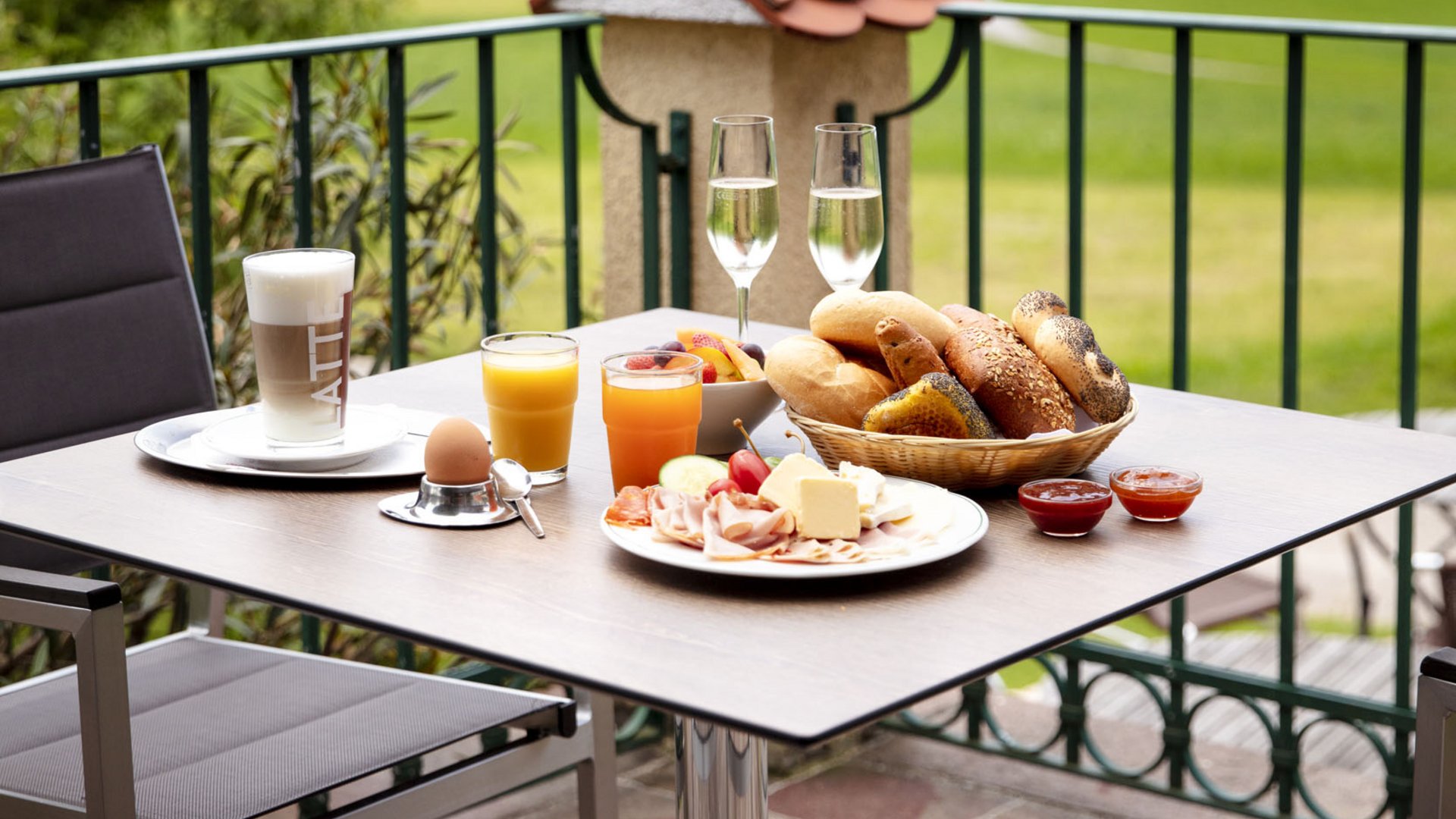 Outdoor breakfast with rolls, drinks, and cold cuts on table with countryside view