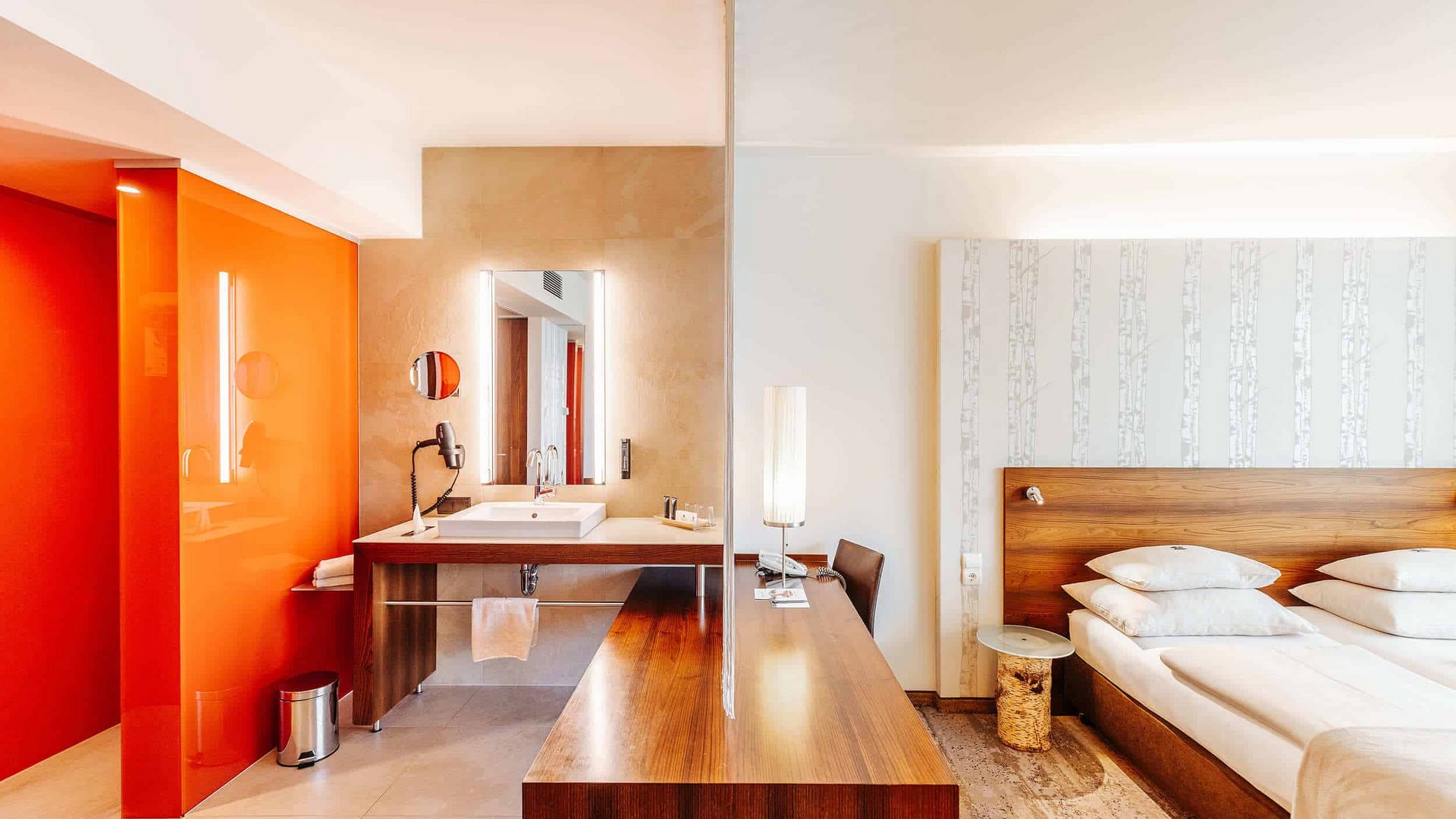 Modern hotel room with wooden furniture and orange accent wall in bathroom