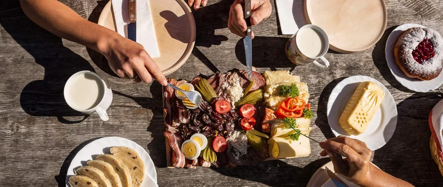 Menschen teilen eine Brotzeit mit Eiern, Käse, Wurst, Marmeladekuchen und Getränken