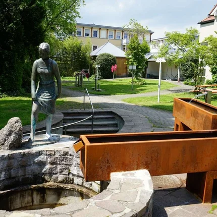 Bronzen beeld naast een historische fontein in een groene stadspark