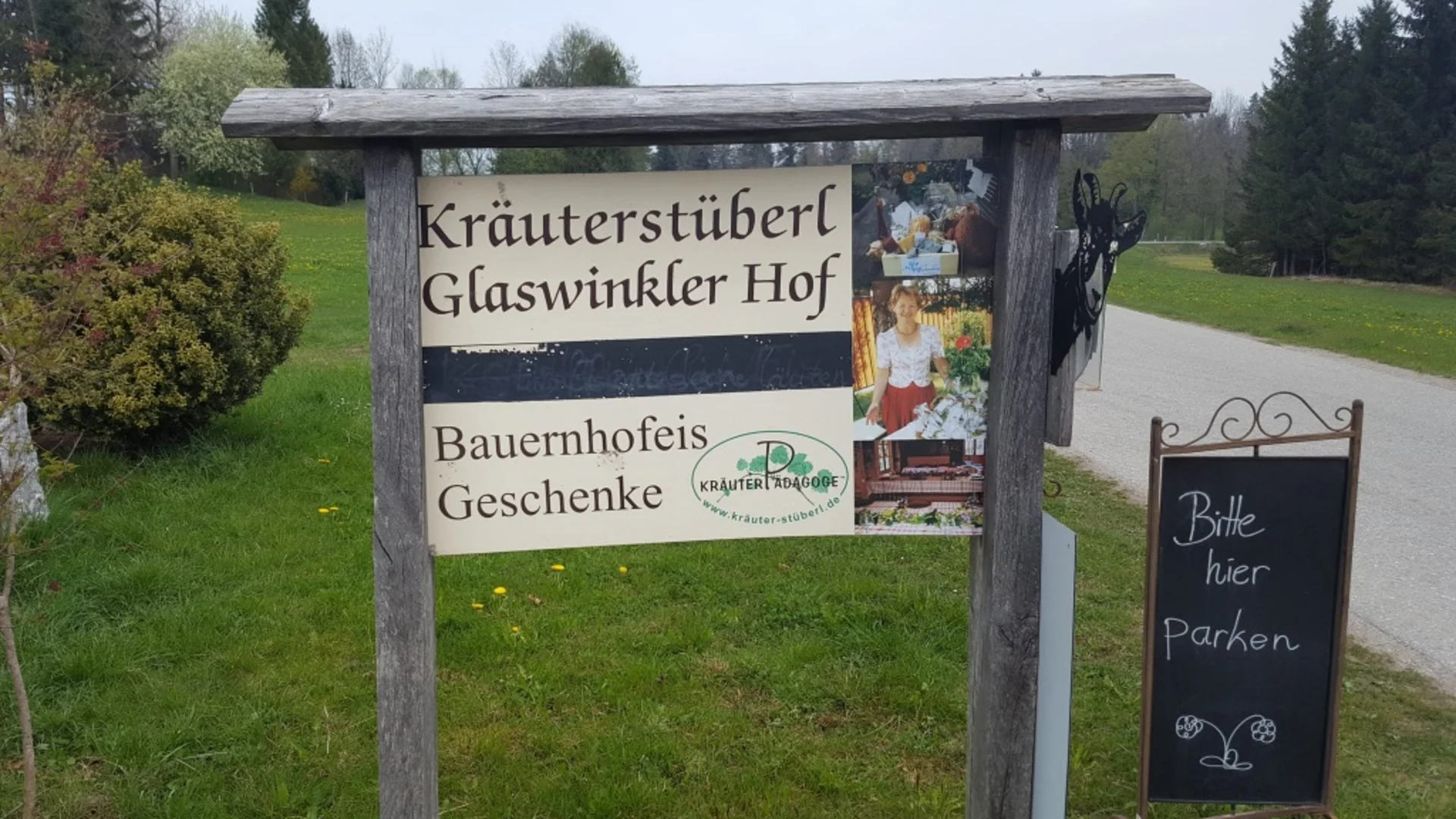 Schild für Kräuterstüberl Glaswinkler Hof mit Parkplatzhinweis auf Wiese neben Straße