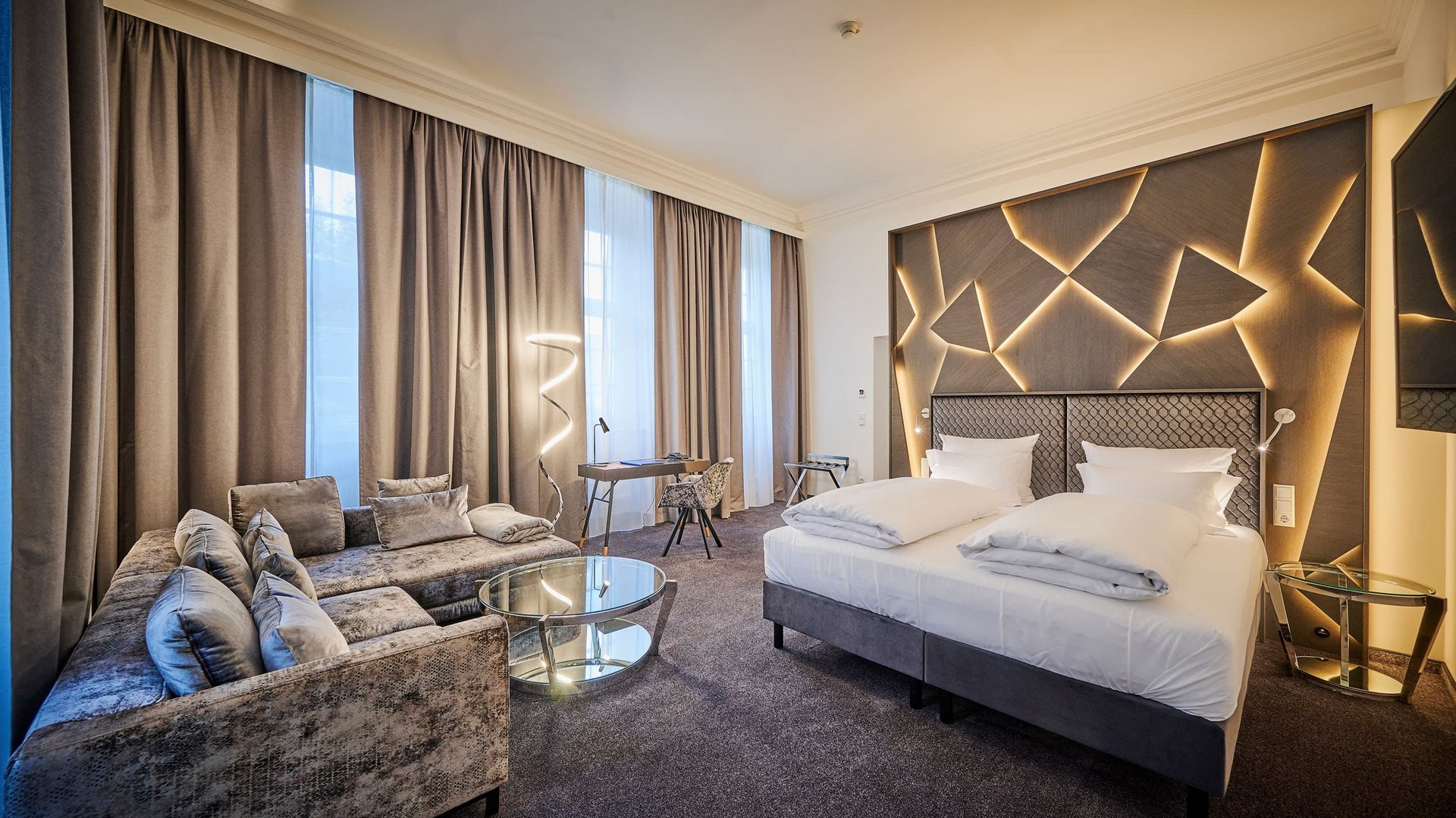 Modern hotel room with double bed, sofa, and decorative illuminated headboard