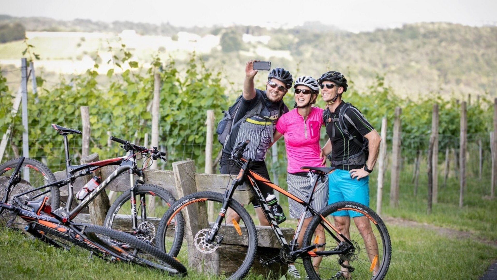 Three cyclists taking a selfie outdoors next to their mountain bikes
