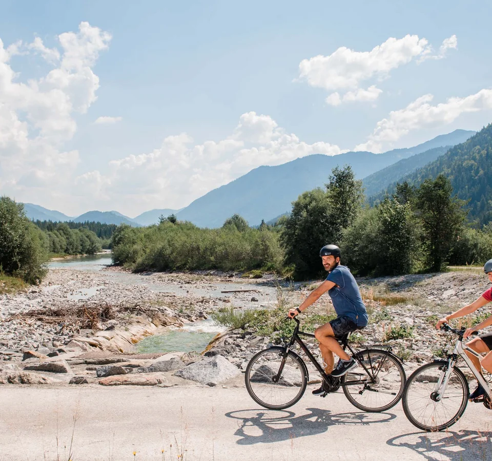 Im Sattel durchs Tölzer Land entlang von Isar & Loisach © Tölzer Land Tourismus - Leonie Lorenz Zwei Radfahrer fahren auf einem Weg neben einem Bach in den Bergen