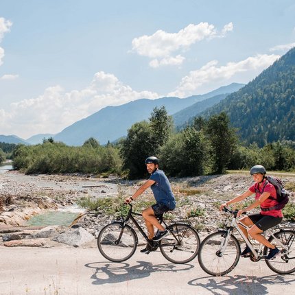 Zwei Radfahrer fahren auf einem Weg neben einem Bach in den Bergen