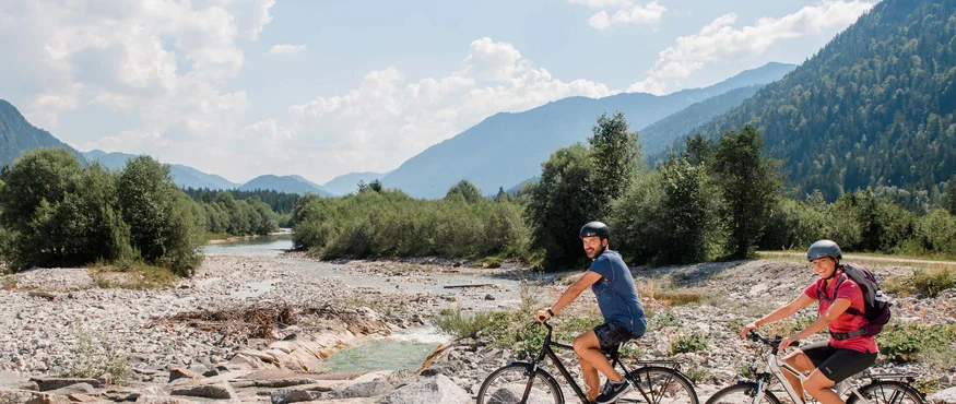 Im Sattel durchs Tölzer Land entlang von Isar & Loisach © Tölzer Land Tourismus - Leonie Lorenz Zwei Radfahrer fahren auf einem Weg neben einem Bach in den Bergen