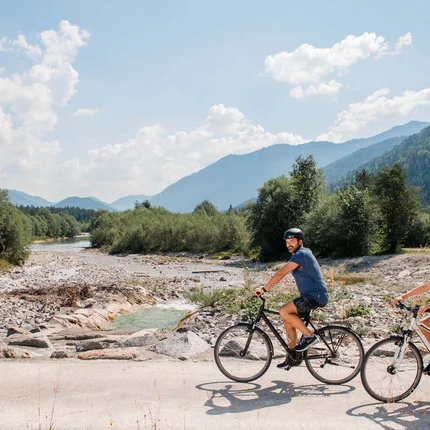 Im Sattel durchs Tölzer Land entlang von Isar & Loisach © Tölzer Land Tourismus - Leonie Lorenz Zwei Radfahrer fahren auf einem Weg neben einem Bach in den Bergen