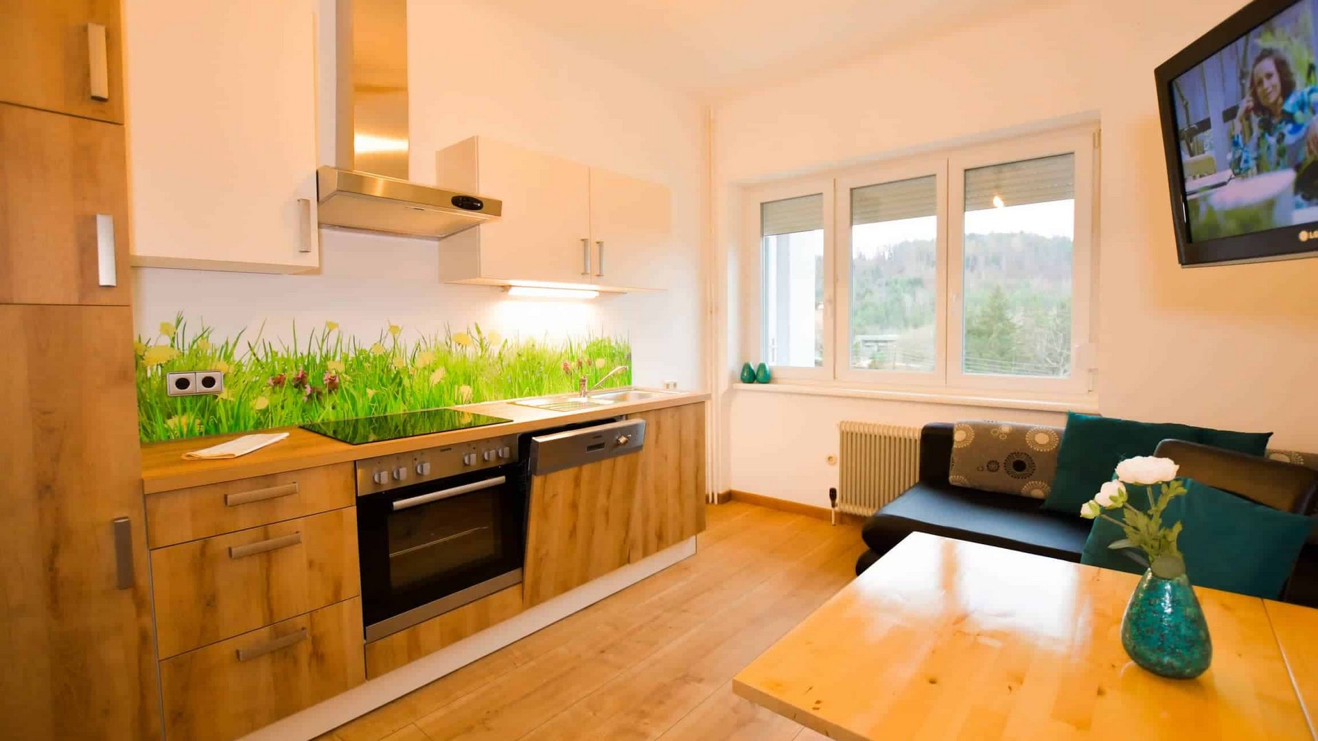 Small modern kitchen with wood cabinets and sofa next to large window