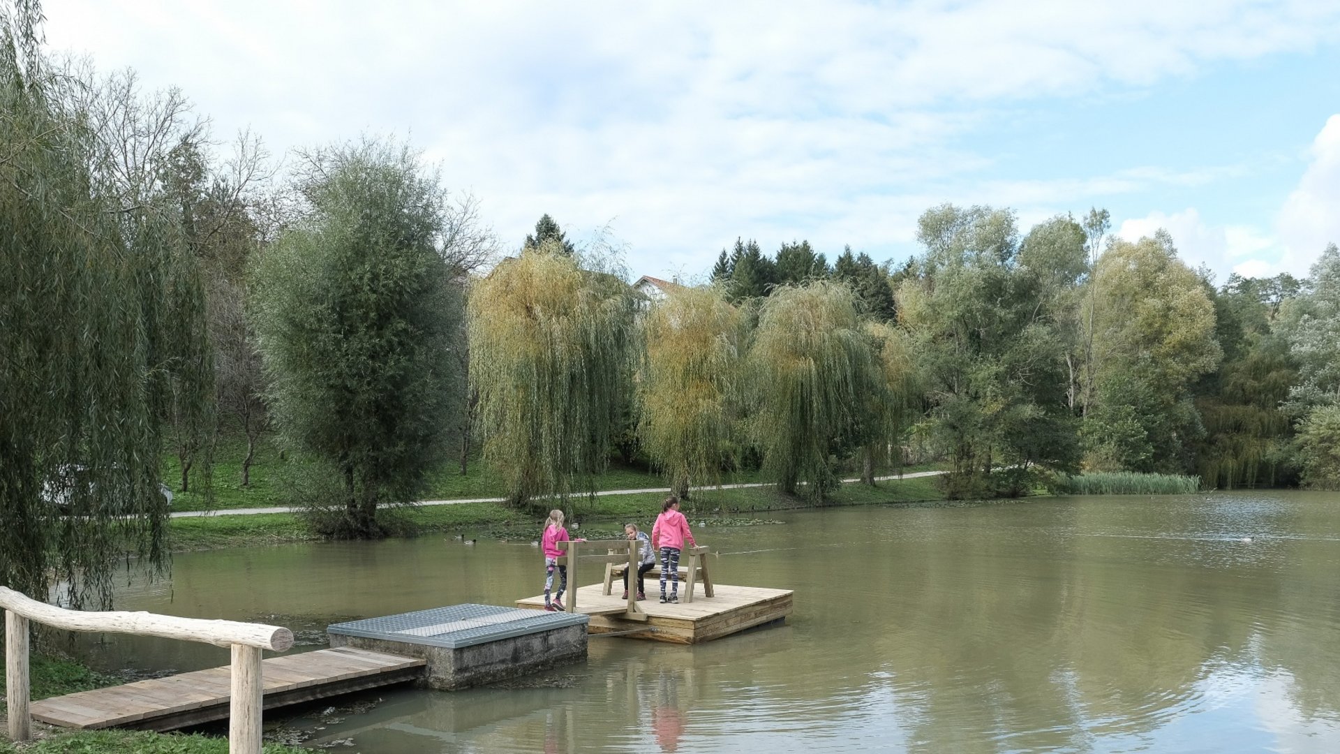 Children on a dock by a lake with trees in the background