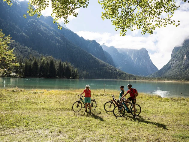 Radreisen in der Gruppe © Velontour Drei Radfahrer an einem Bergsee mit bewaldeten Bergen im Hintergrund