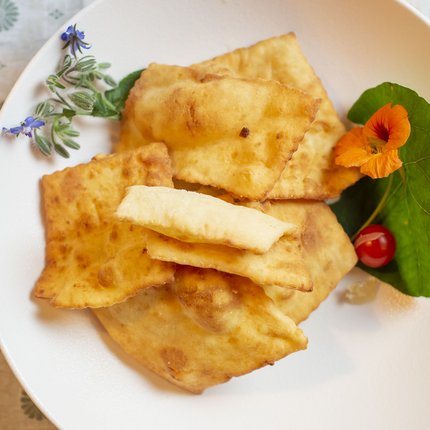 Fried dough pieces on white plate garnished with edible flower and herbs