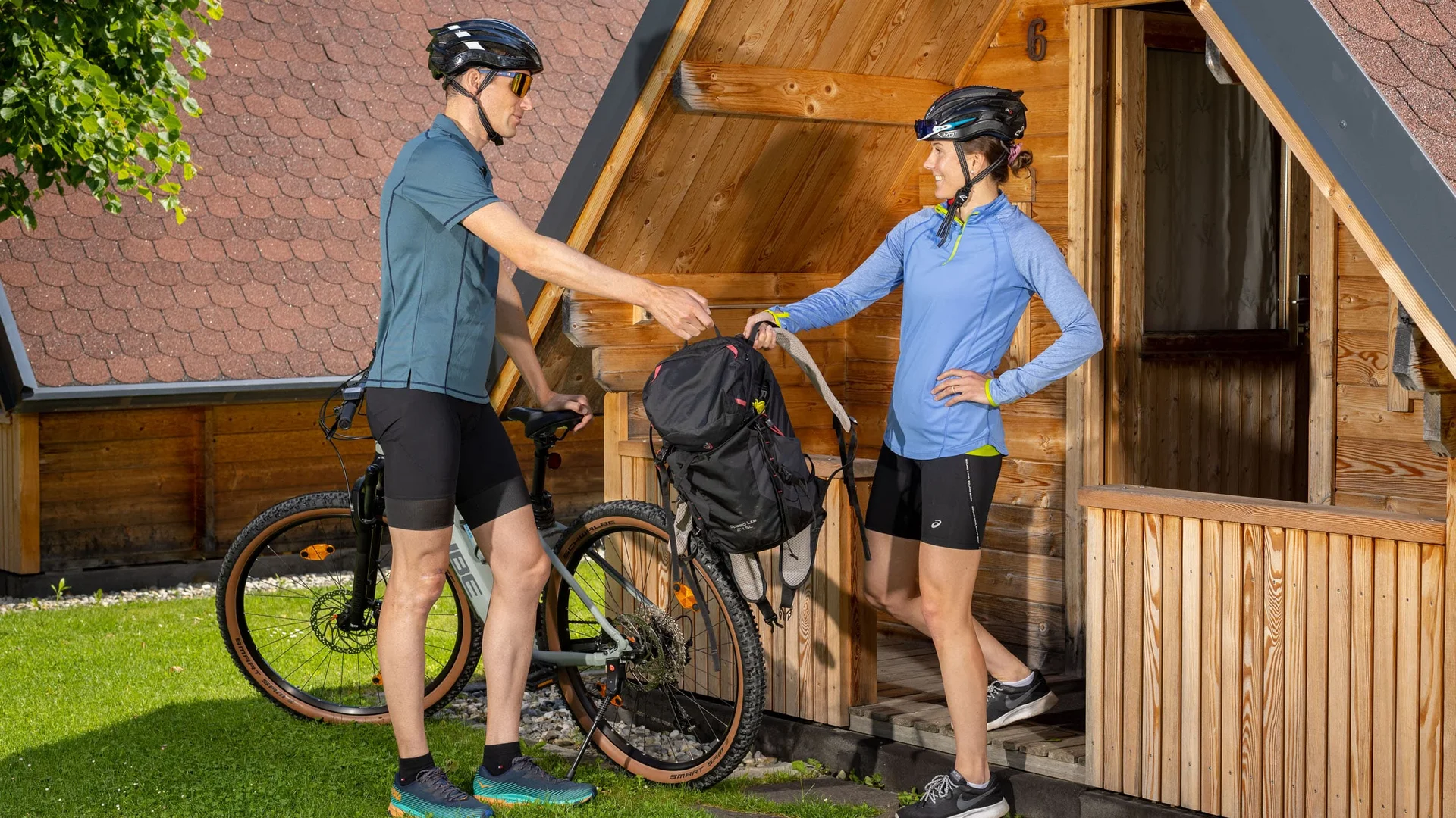 Twee fietsers wisselen rugzak uit bij houten hut