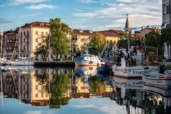 Grado: Herbst-Radeln an der Adria © Mario Callegari Boote am Kanal mit Gebäuden und Bäumen, Spiegelung im Wasser