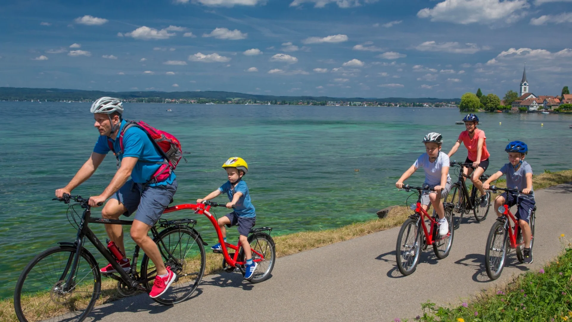 Family cycling along a lakeside path on a sunny day