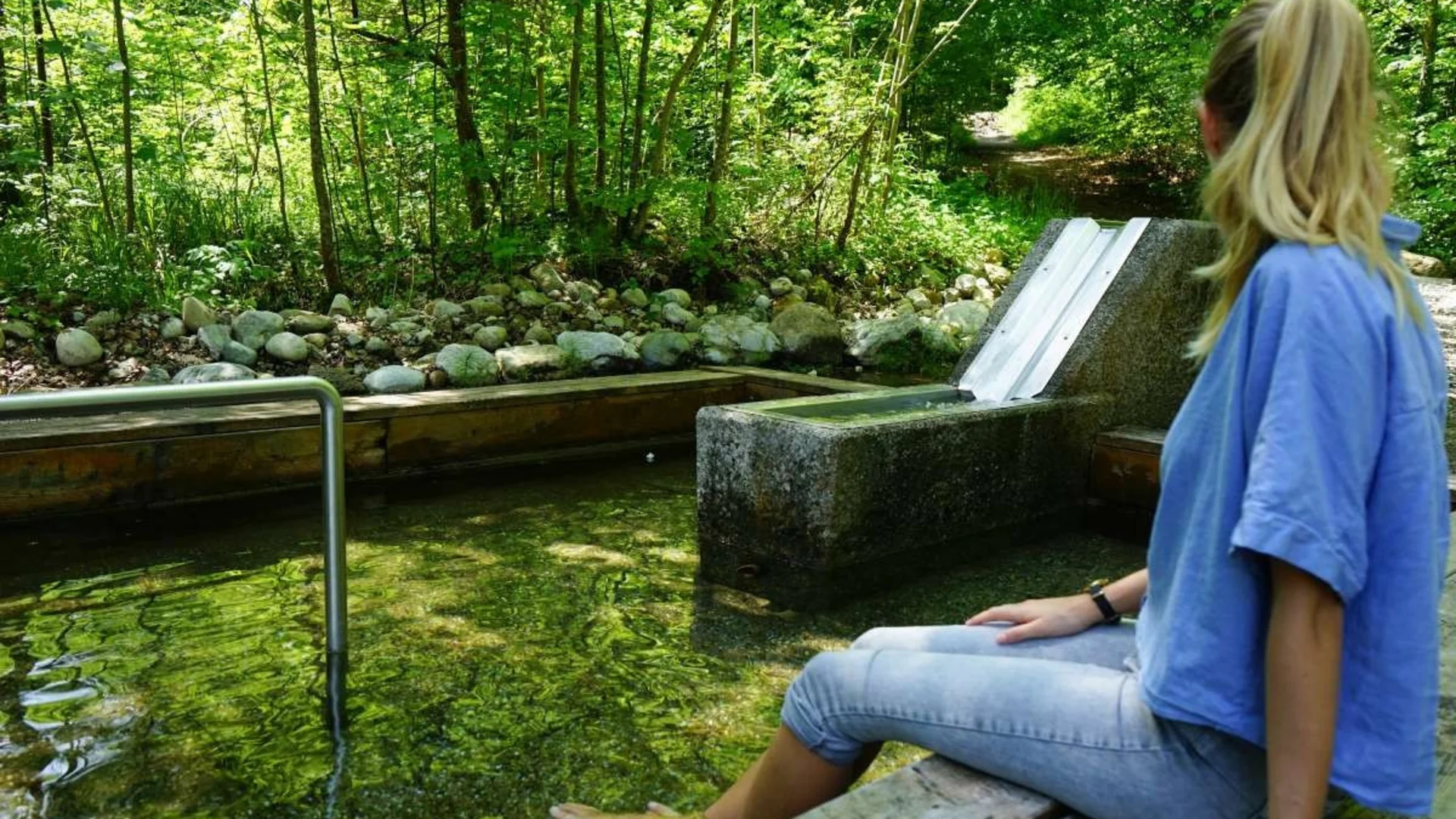 Vrouw zit met blote voeten in eenheldere bron in het bos