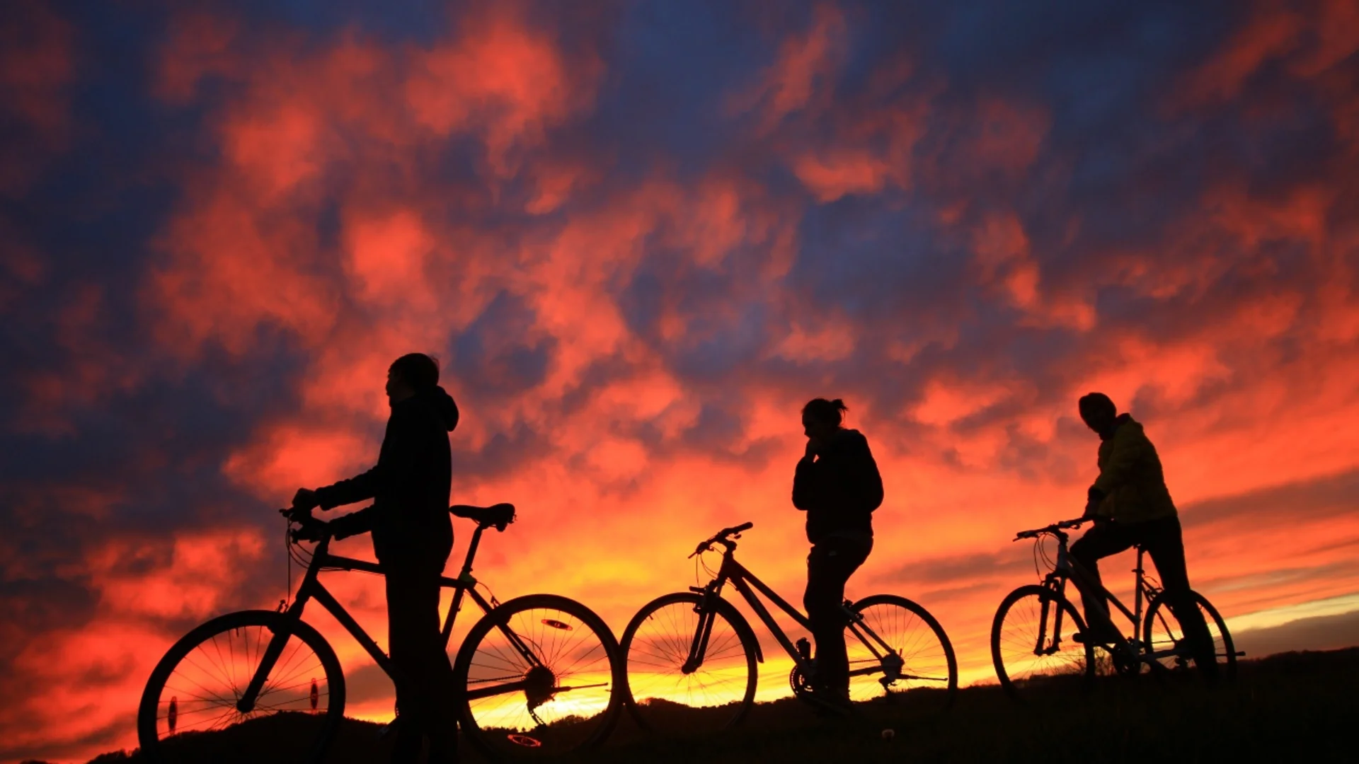 Drie mensen met fietsen als silhouet tegen een dramatische zonsondergang