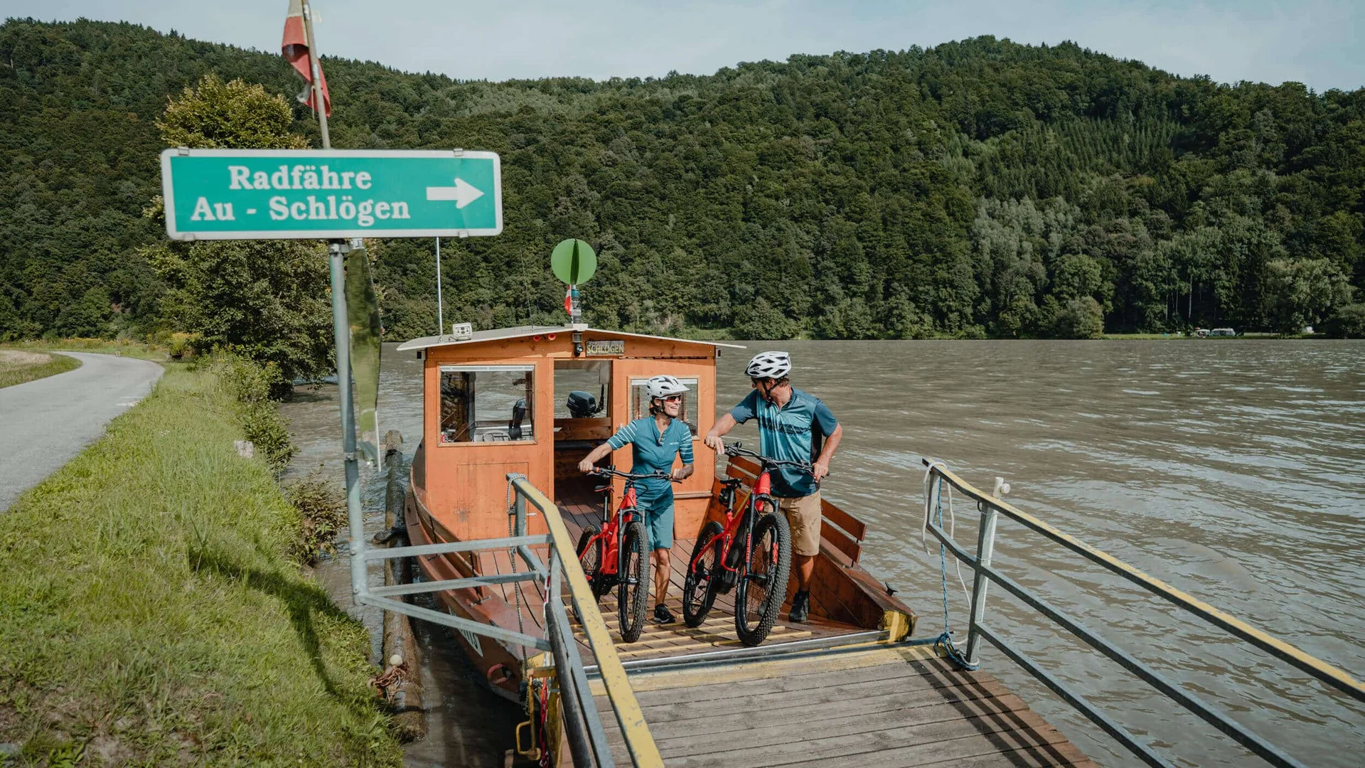 Zwei Radfahrer mit Fahrrädern auf einer kleinen Fähre auf einem Fluss
