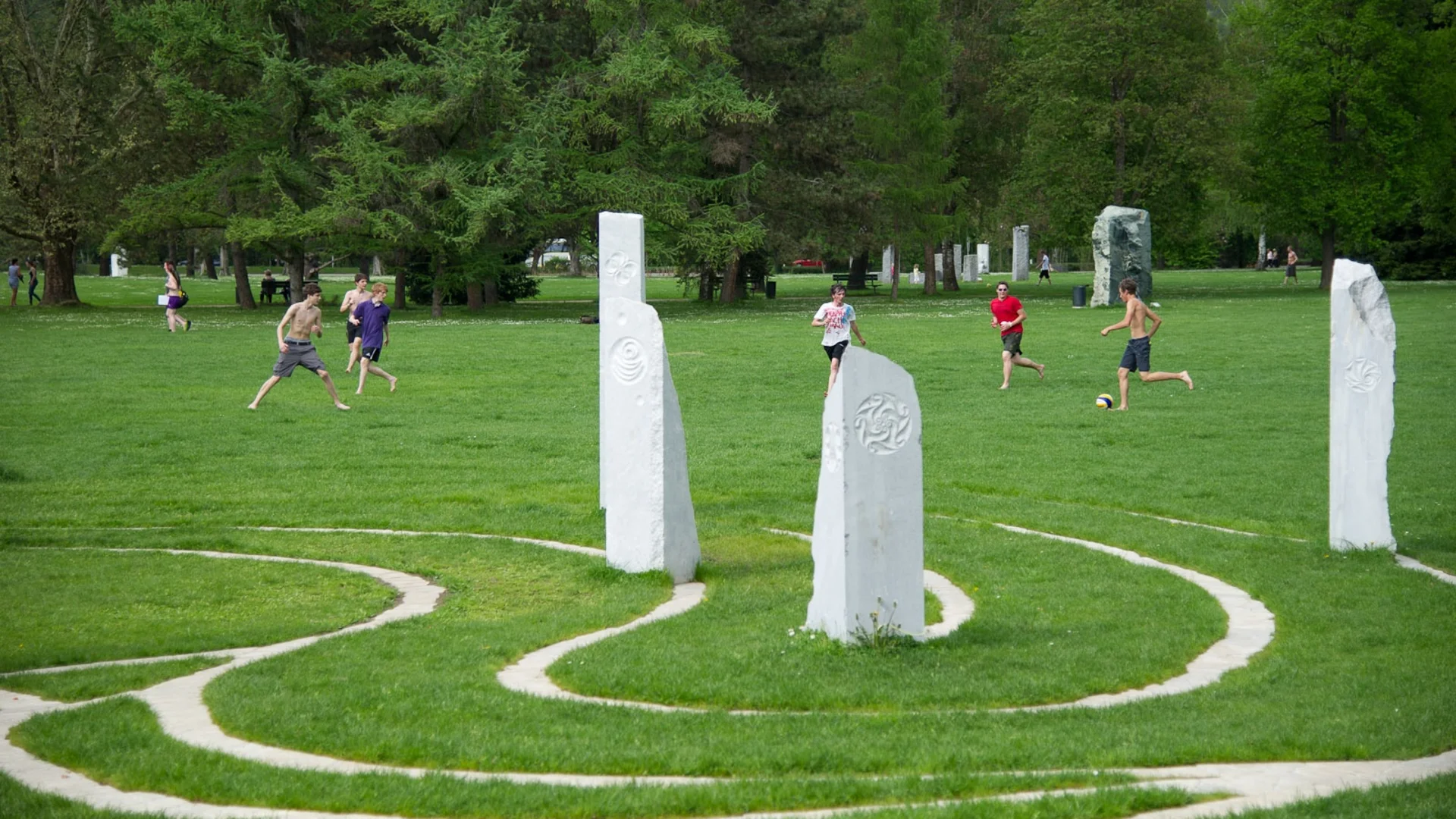 Jongens spelen voetbal op grasveld bij witte stenen pilaren in park