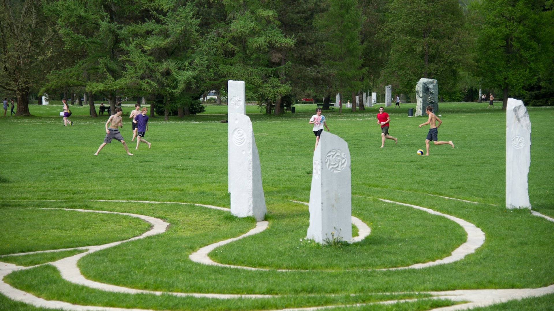 Boys playing soccer on grass near white stone pillars in park