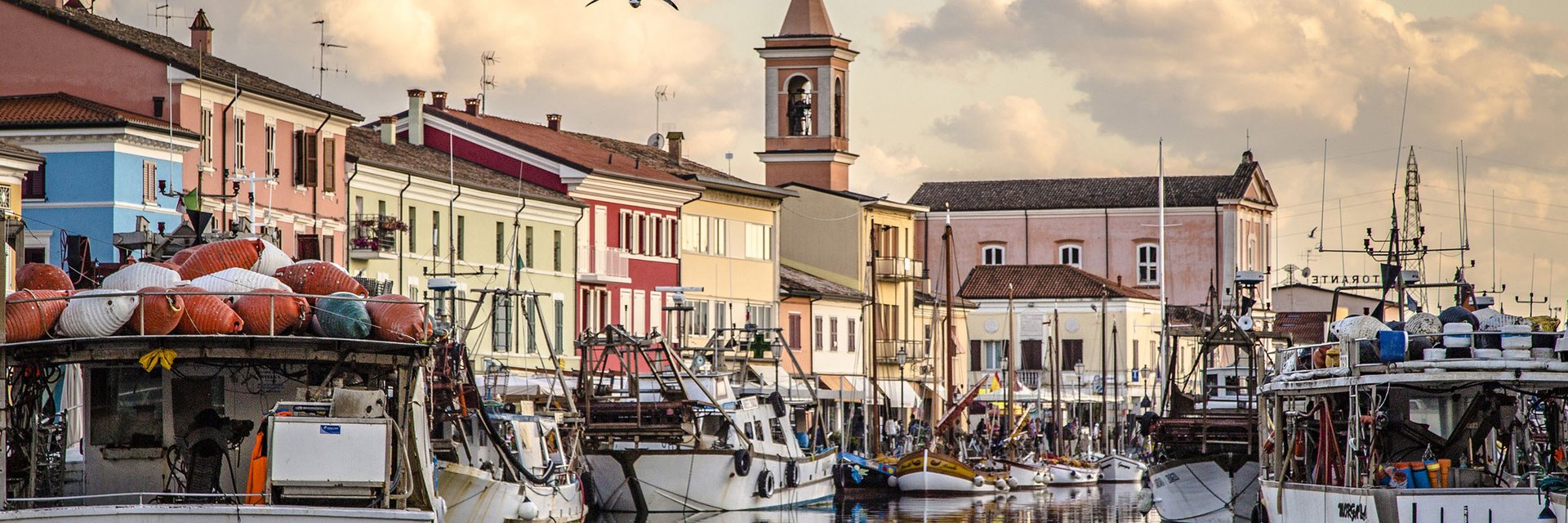 Fishing boats docked along colorful houses and a church at sunset