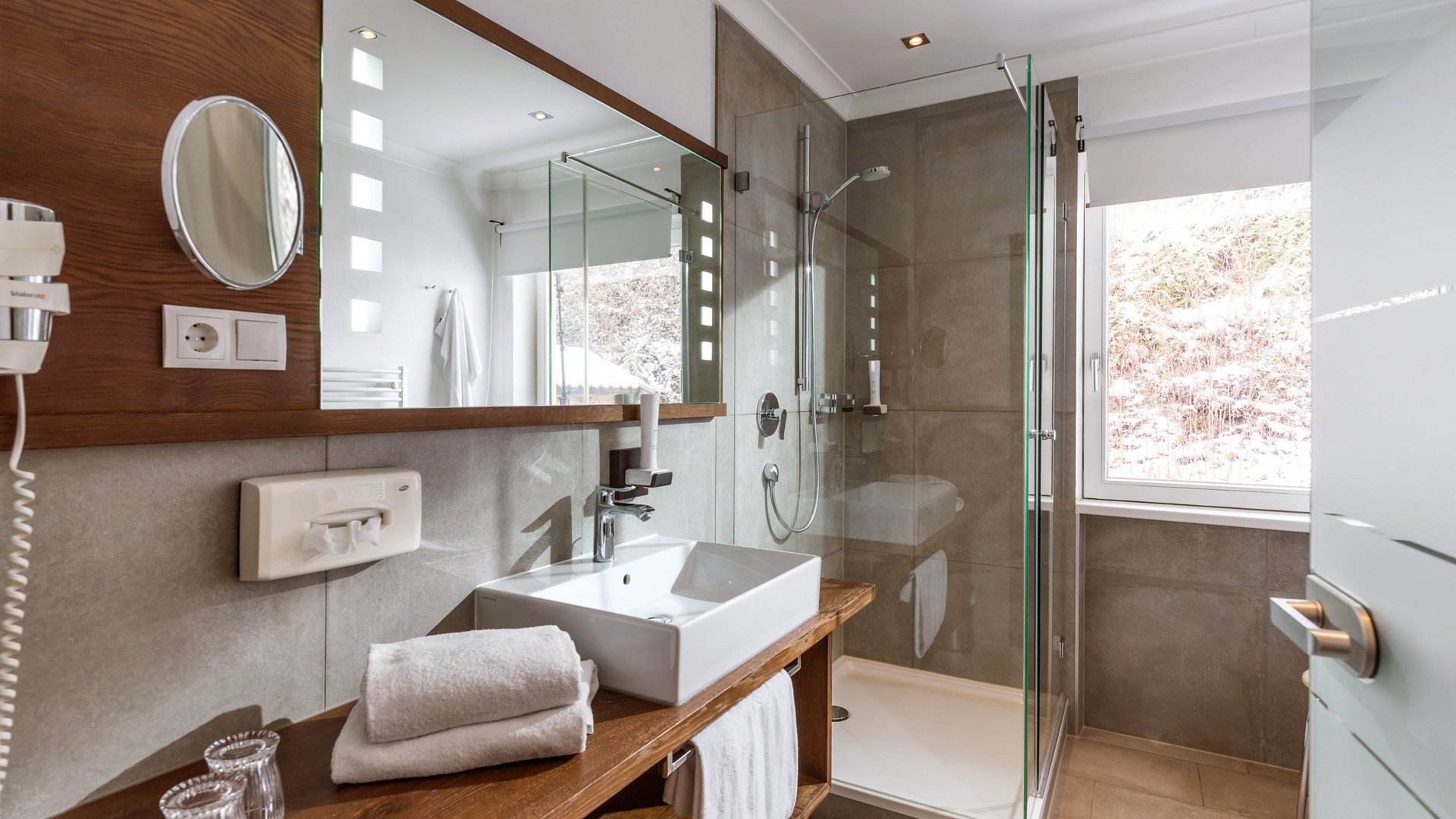 Modern bathroom with wooden shelf, white sink and glass shower
