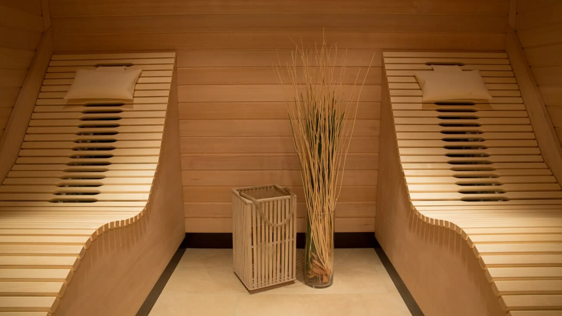 Twee houten ligstoelen met kussens in een houten saunaruimte