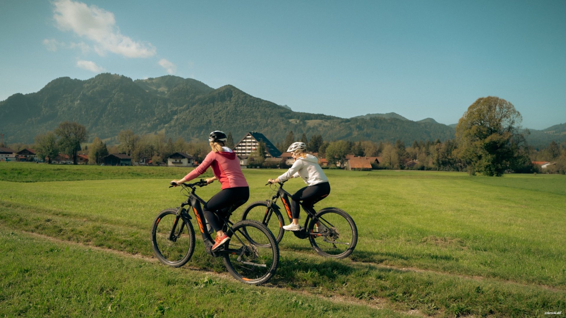 Two cyclists riding on a dirt path with mountains in the background