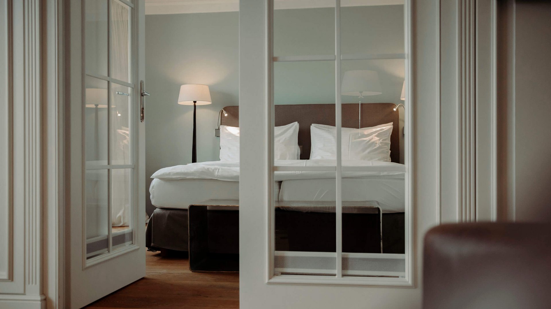 View through glass door of cozy double bed with lamp in modern bedroom