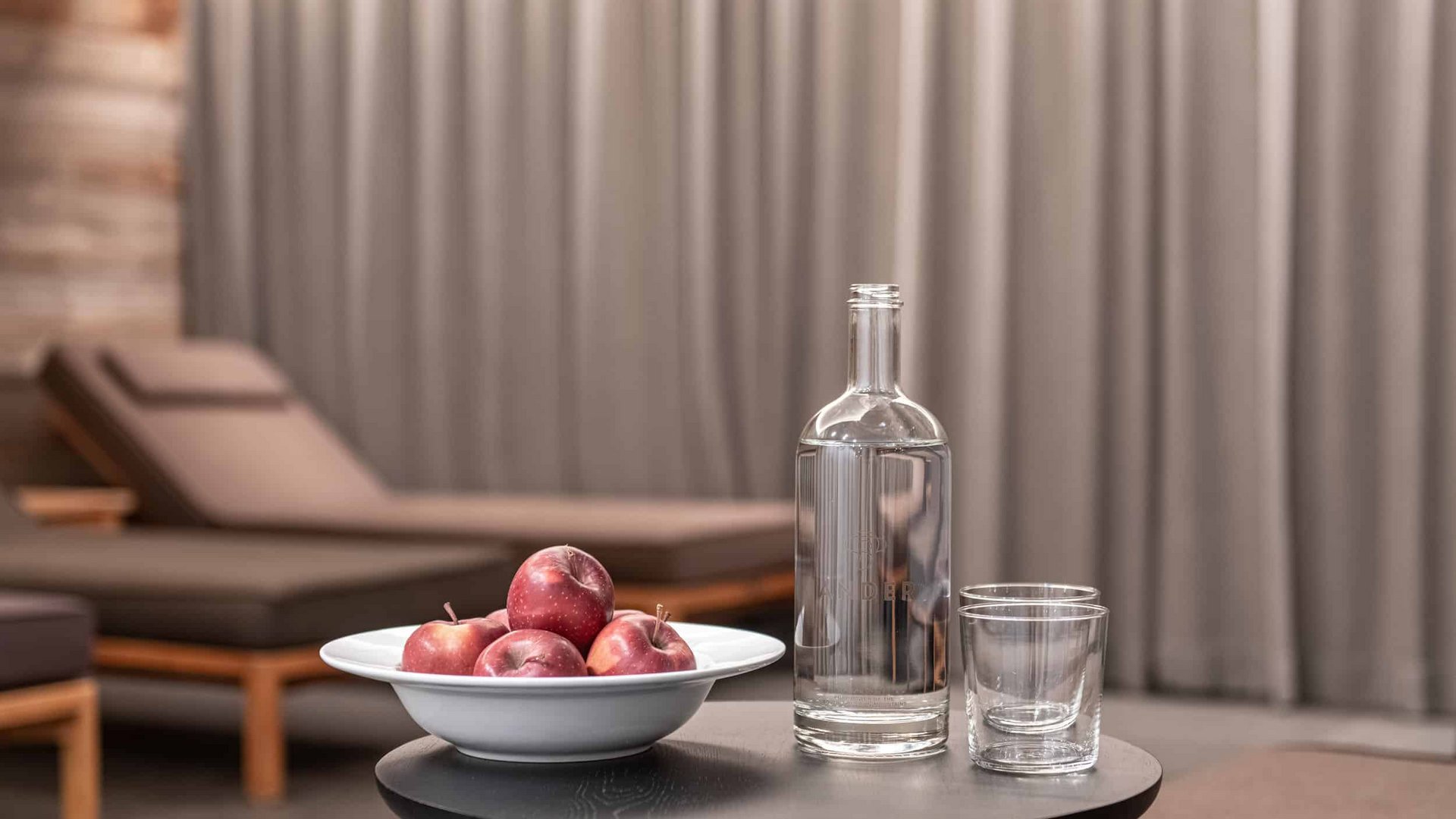 Glass bottle and apples on a small table near lounge chairs