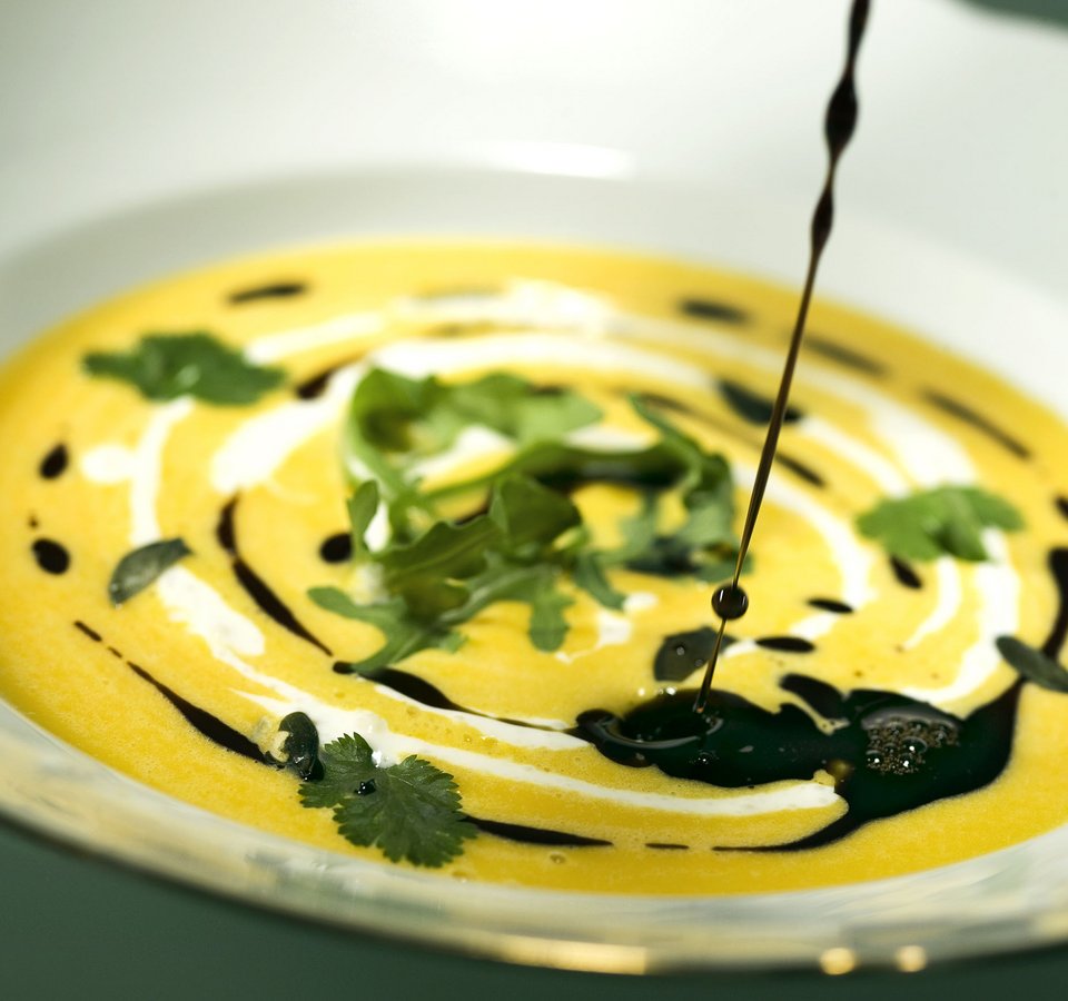 Pumpkin soup with cream, herbs, and dark oil in white bowl