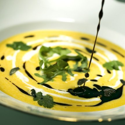 Pumpkin soup with cream, herbs, and dark oil in white bowl