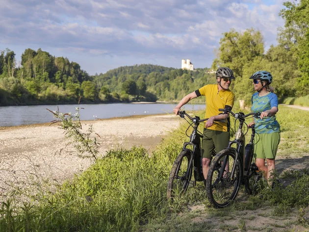 7 Quellen der Entschleunigung © Velontour - Heiko Mandl Zwei Radfahrer stehen mit Fahrrädern am Flussufer vor bewaldeten Hügeln