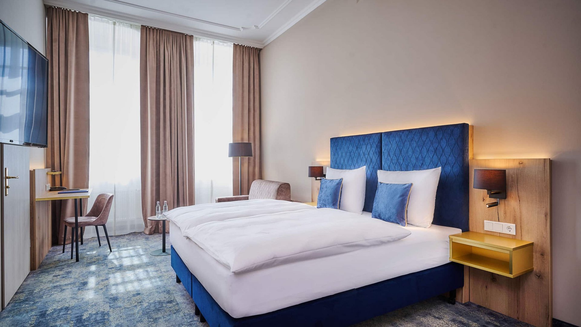 Modern hotel room with large bed, blue accents, and bright natural light