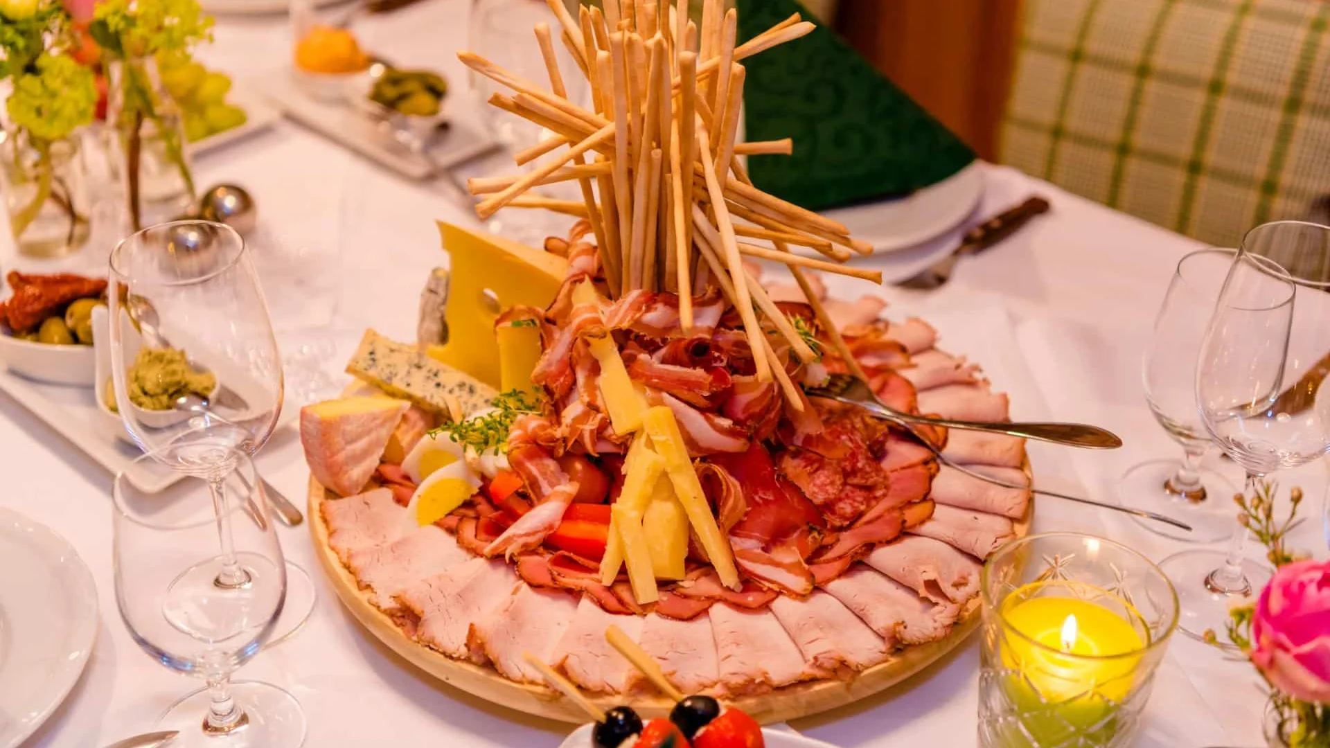 Uitgebreide schaal met vleeswaren, kaas en broodstengels op feestelijk gedekte tafel