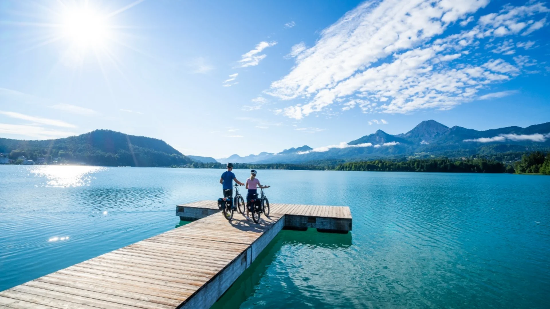 Twee fietsers op een steiger met uitzicht op meer en bergen bij zonnig weer