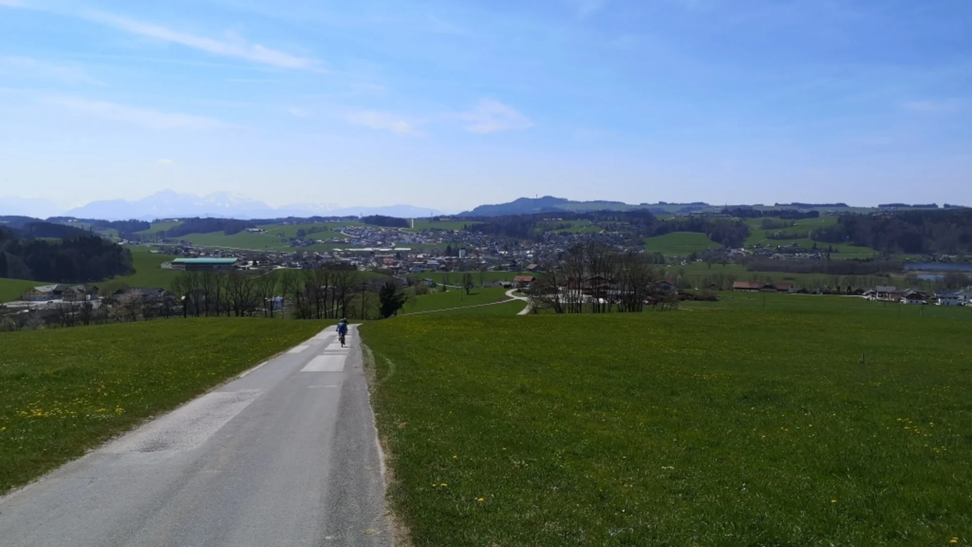 Tour-Detail © Bettina Bauer Fahrradfahrer auf Straße durch grüne Felder mit Stadt und Bergen im Hintergrund