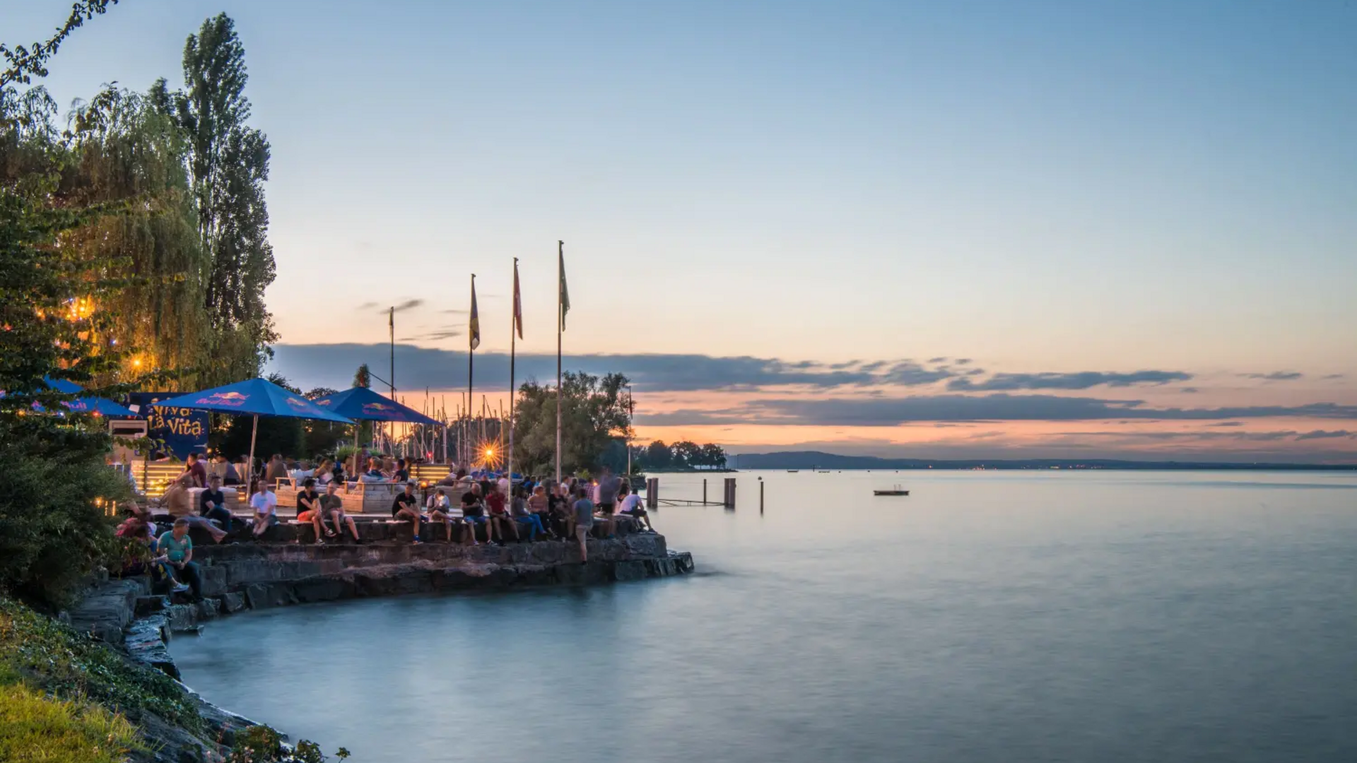 People sitting on lakeside pier at sunset with calm water