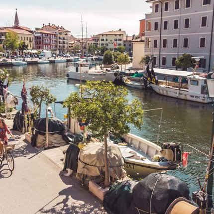 Two cyclists ride along a canal with boats and colorful buildings in the city