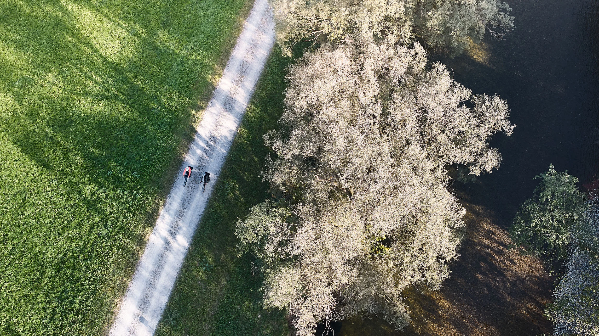 Twee fietsers op een pad naast een boom en water, luchtfoto